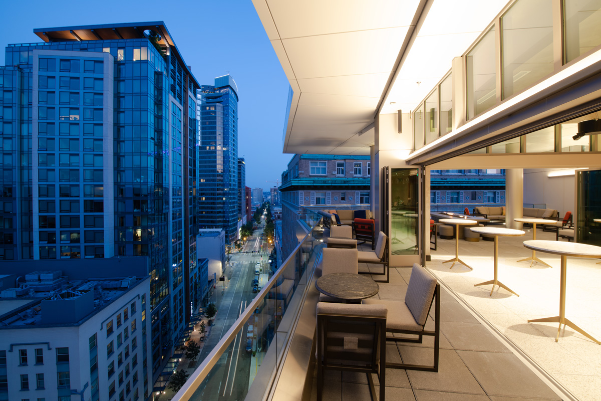 A balcony with outdoor seating and a city view at dusk.
